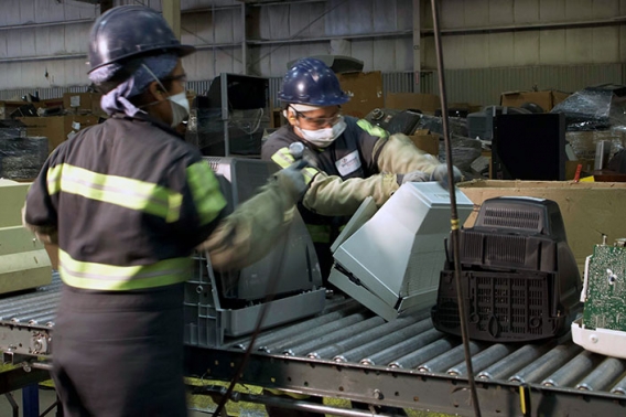 Workers in protective gear handle recycled products as they move down a conveyor line